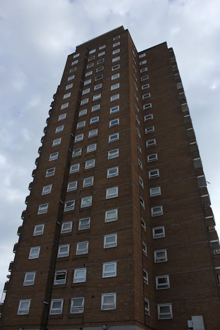 The image shows a curved residential street lined with multi-storey brick apartment buildings with black metal balconies. The pavement features a wide sidewalk with a tactile paving strip near the cur
